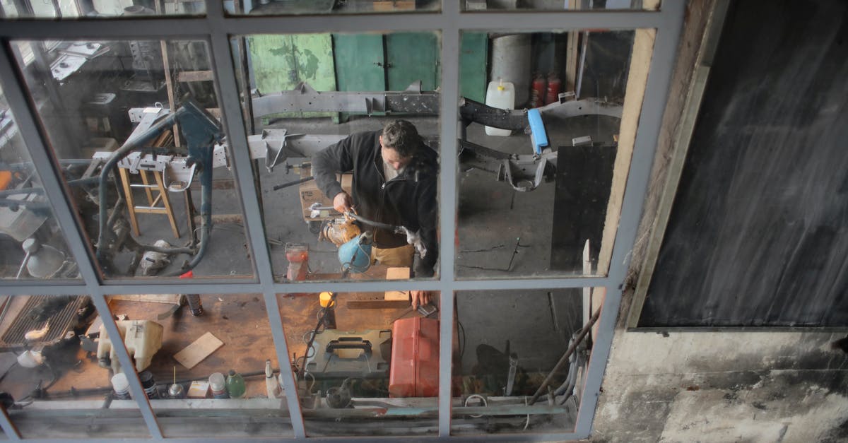 Unable to trade or battle pokemon, how to fix? - Through window view of male worker in casual uniform standing near workbench and working with instruments in grungy workshop Unable to trade or battle pokemon, how to fix? - Through window view of male worker in casual uniform standing near workbench and working with instruments in grungy workshop