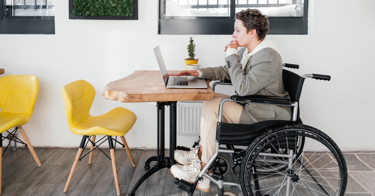 Uncharted - Disable puzzle hints from Sully - Full body side view of focused disabled female freelancer browsing internet on netbook while sitting at table during online work in cafeteria