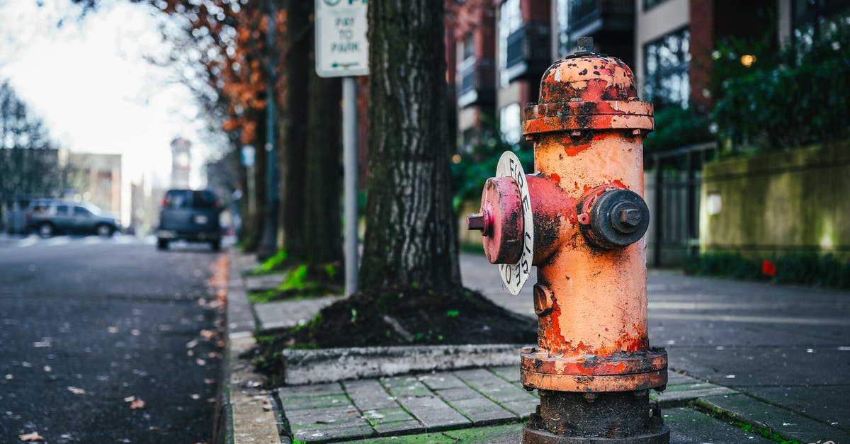 Undo path that leads to $20 DLC purchase on Fire Emblem Fates - Old metal rusty fire hydrant placed near asphalt roadway on street with residential houses and tall trees on blurred background