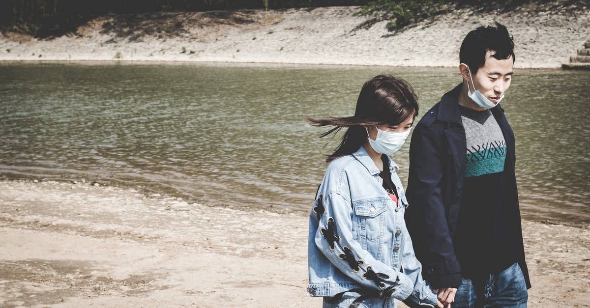 Unlock a redstone repeater after a period of time - Asian couple in masks holding hands while walking near river Unlock a redstone repeater after a period of time - Asian couple in masks holding hands while walking near river