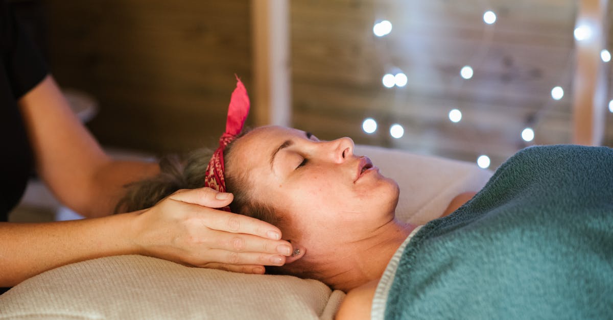 Unlocking the alternative side-quests? - Side view of relaxed female patient with closed eyes lying on table under blanket while getting massage reiki during healing session in salon
