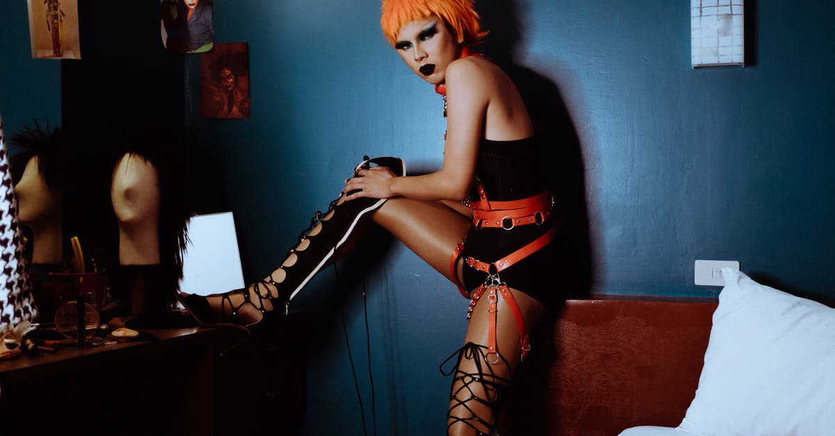 Unlocking the alternative side-quests? - Side view unemotional extravagant female with orange dyed hair and dark makeup wearing bodysuit and thigh high shoes putting leg on vanity table and looking at camera Unlocking the alternative side-quests? - Side view unemotional extravagant female with orange dyed hair and dark makeup wearing bodysuit and thigh high shoes putting leg on vanity table and looking at camera