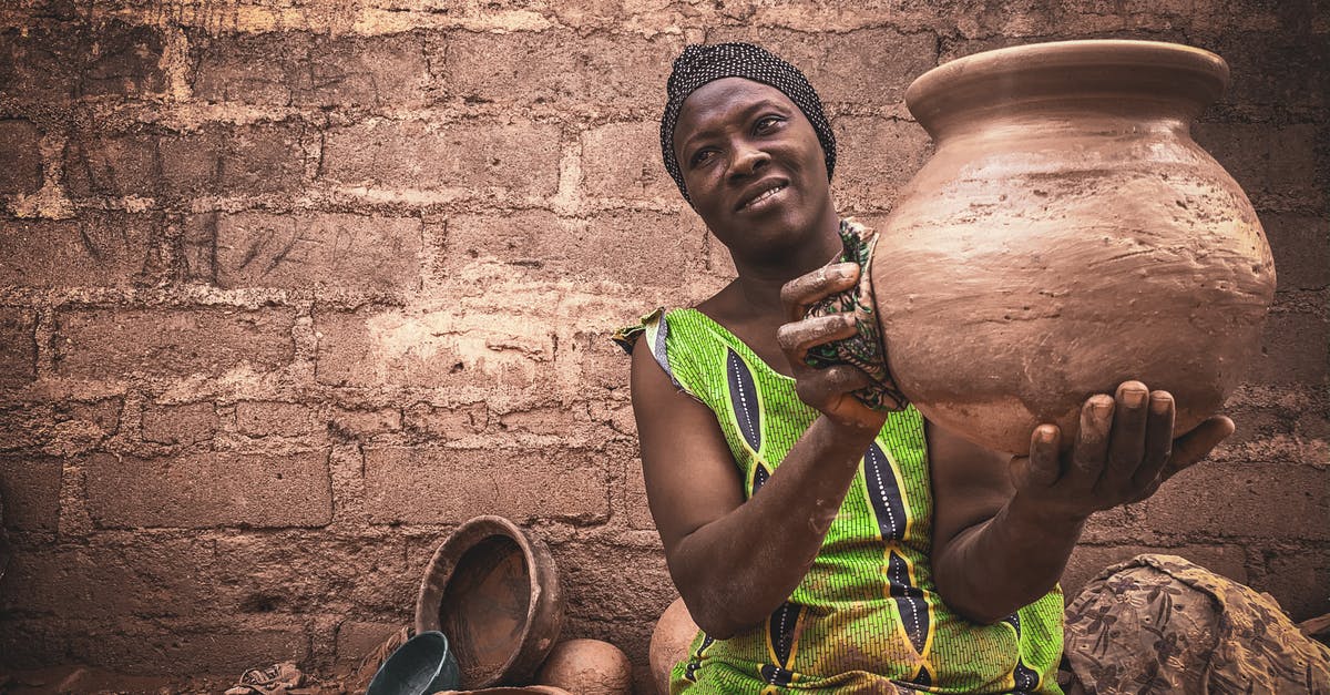 Use of outdoorsman skill at local map - Smiling middle aged ethnic female in traditional dress and turban demonstrating handmade clay pot while sitting on street against shabby wall Use of outdoorsman skill at local map - Smiling middle aged ethnic female in traditional dress and turban demonstrating handmade clay pot while sitting on street against shabby wall