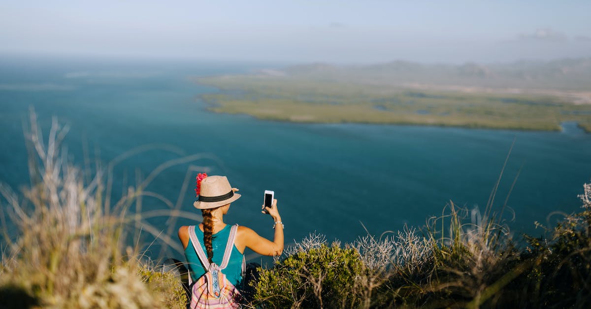 Using AXII when mounted - Back view of unrecognizable female traveler taking photo of foggy ocean on cellphone while resting on grass mount