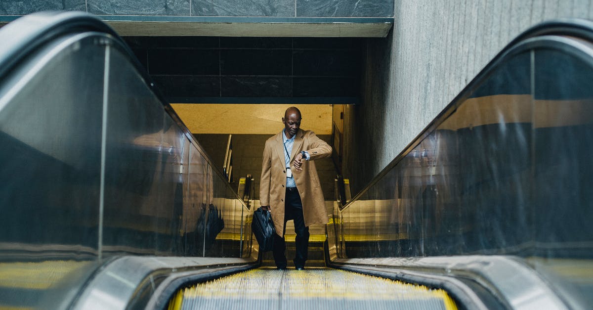 Vessels escaping host bodies over time - Contemplative black businessman riding escalator and looking at wristwatch Vessels escaping host bodies over time - Contemplative black businessman riding escalator and looking at wristwatch