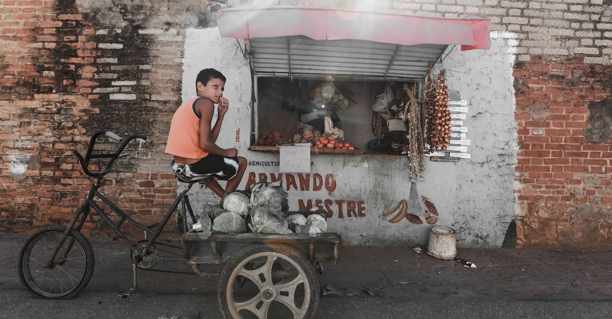 Vilified by community in Original Fallout? - Ethnic boy sitting on aged tricycle near poor street stall Vilified by community in Original Fallout? - Ethnic boy sitting on aged tricycle near poor street stall
