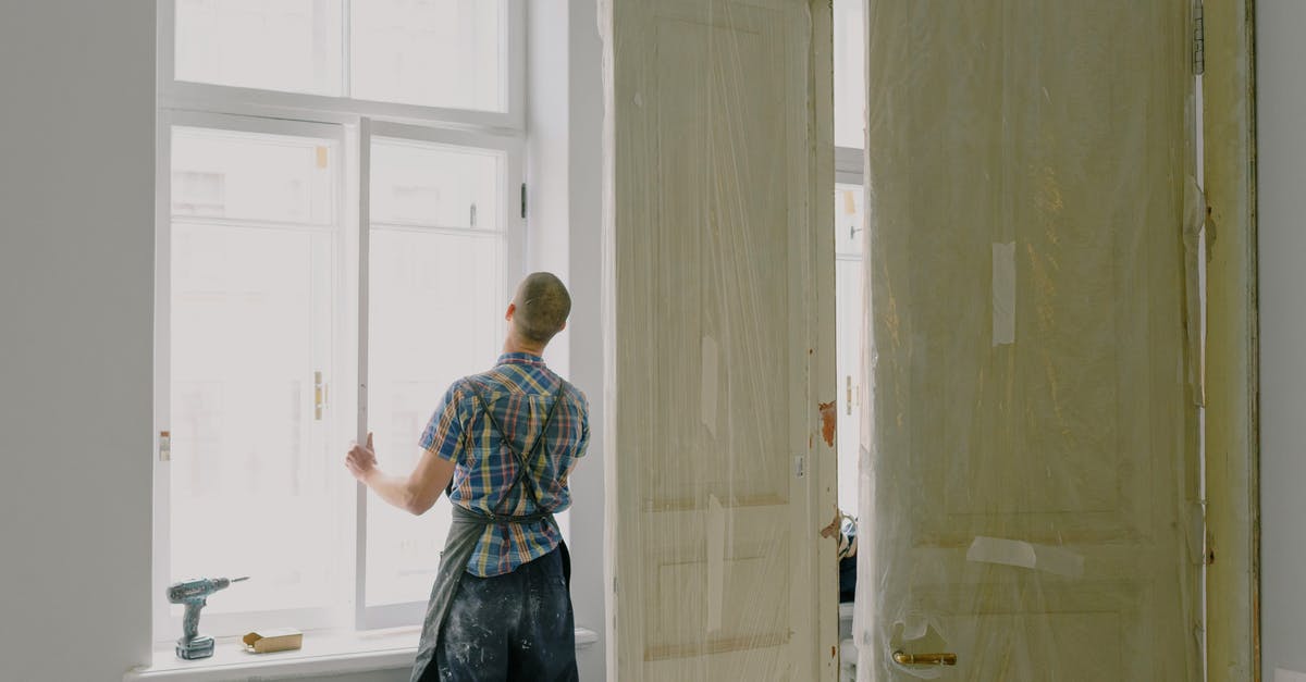 Visiting New Zealand, unable to install - Back view of unrecognizable workman in apron mounting window near drilling machine and doors in flat Visiting New Zealand, unable to install - Back view of unrecognizable workman in apron mounting window near drilling machine and doors in flat