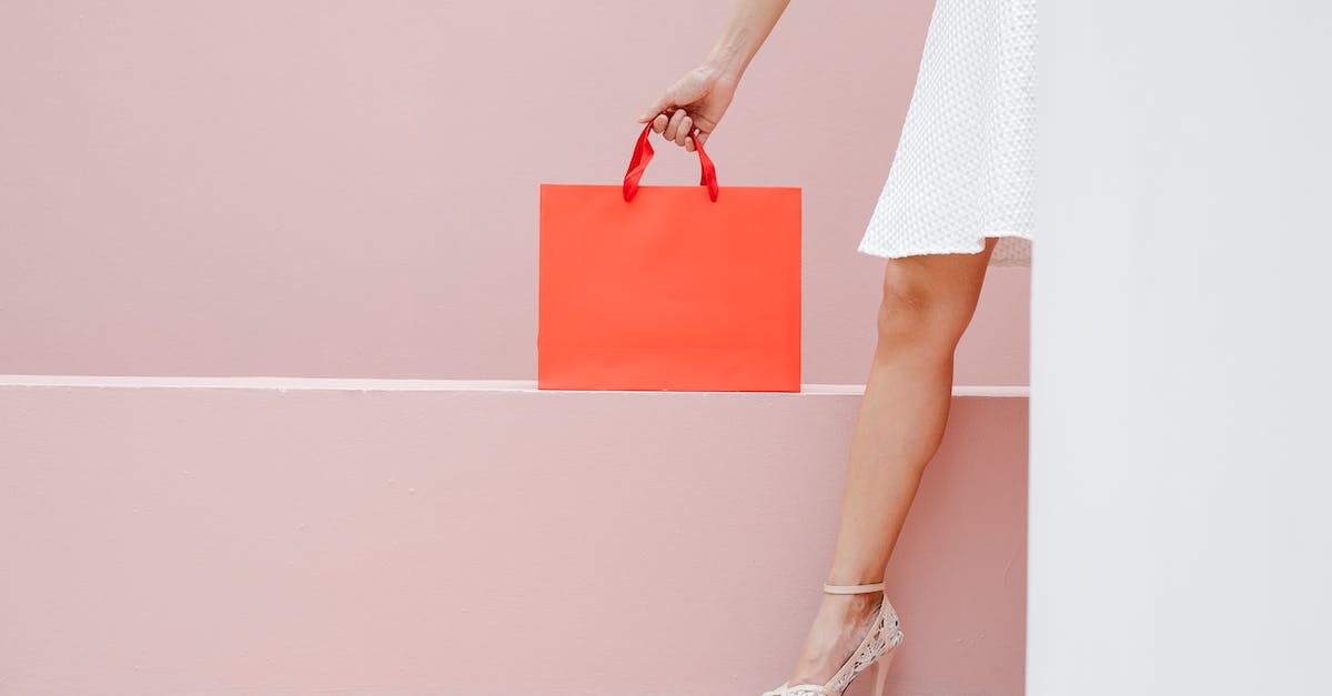 Was I supposed to get something extra for my first store purchase? - Crop anonymous stylish female in white dress and high heels carrying red shopping bag against pink wall
