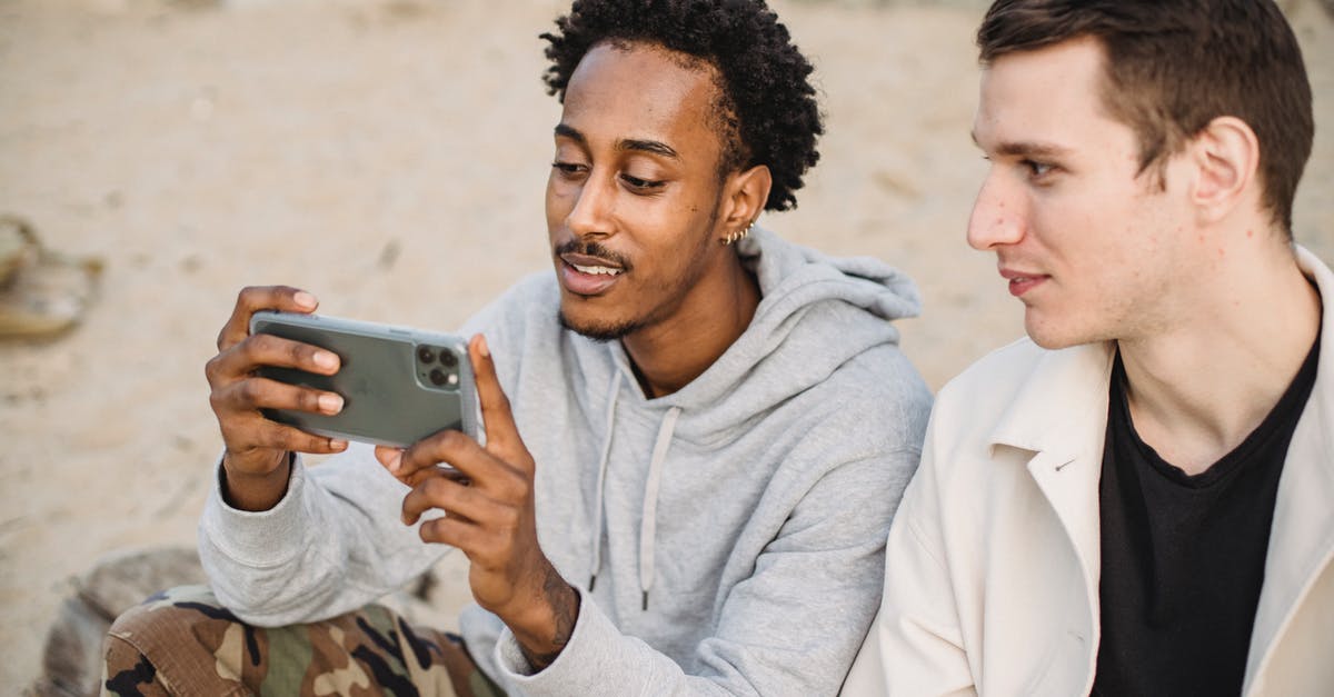 Watch won't show time - Attentive African American male sharing mobile phone with friend and watching video on sandy ground Watch won't show time - Attentive African American male sharing mobile phone with friend and watching video on sandy ground