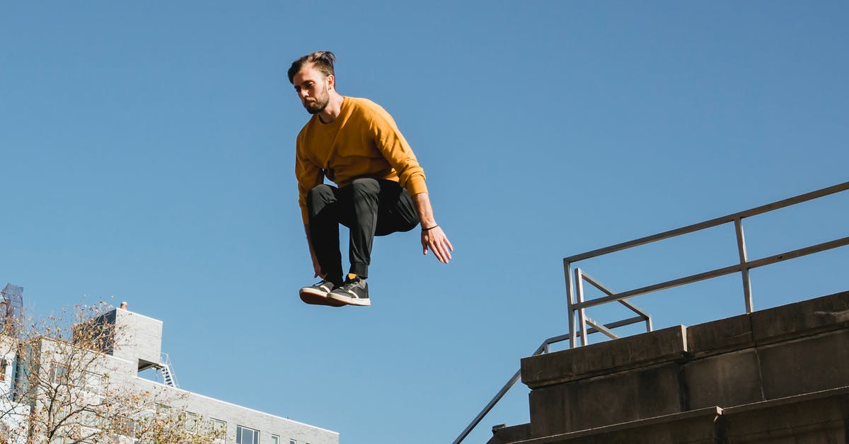 Weird 4 tile jump height in Terraria - Low angle of young male athlete performing parkour jump on building under clear blue sky
