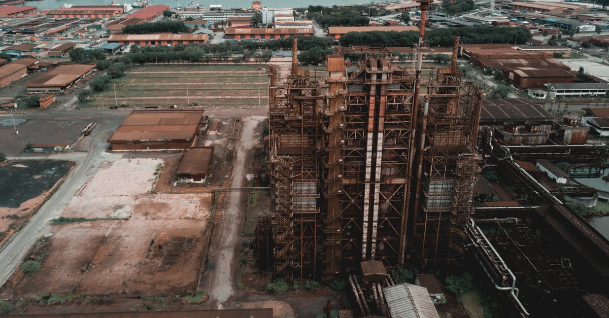 What's more eco-friendly: Steel furnaces or Electric furnaces? - Aerial view of factory with shabby buildings and rusty industrial constructions located in harbor of city