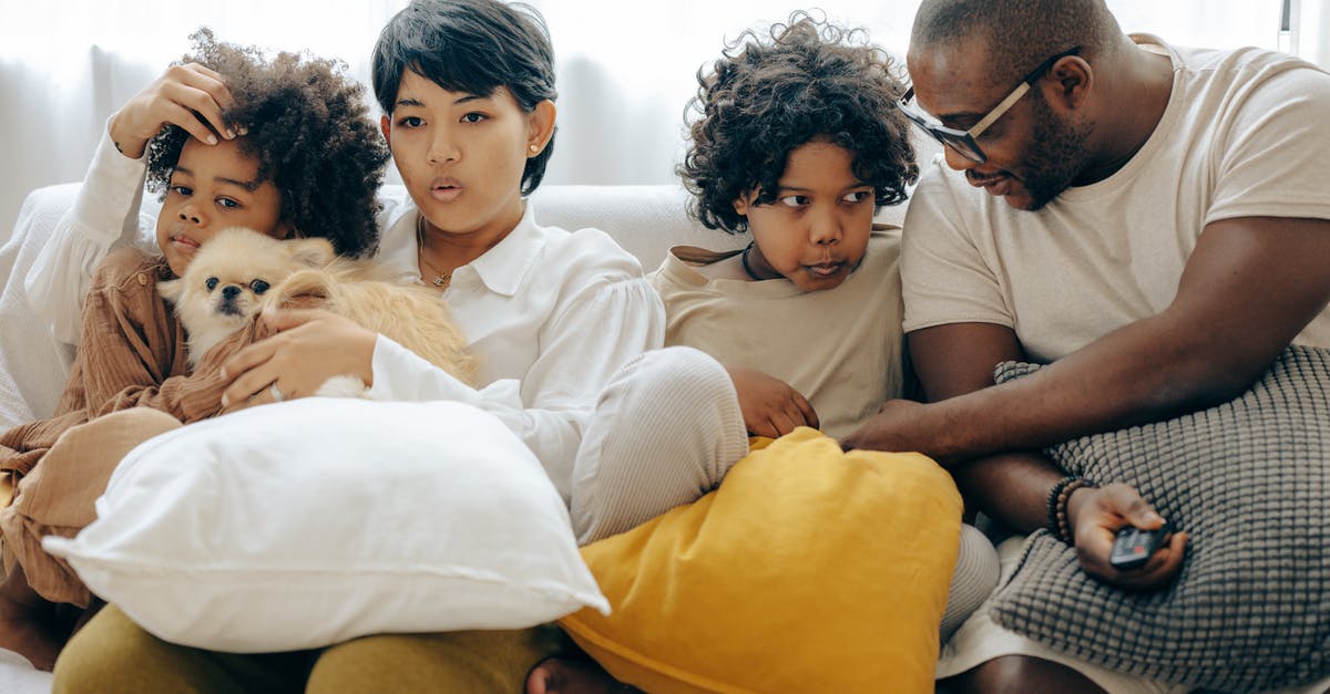 What's the best way to annihiliate an enemy's family? - Multiracial family resting on comfortable sofa together with little dog while mother and little son watching TV with interest and father and elderly son talking to each other