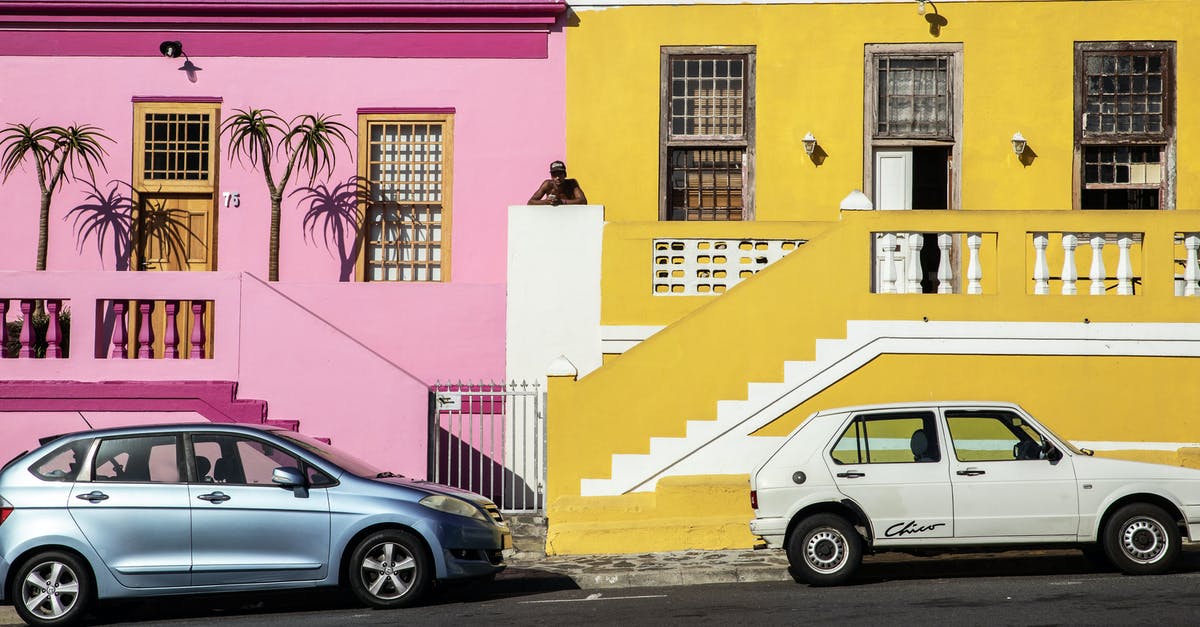 What's the difference between paint jobs and variants? - Distant African American man standing between pink and yellow residential buildings located near road with parked cars on street in town