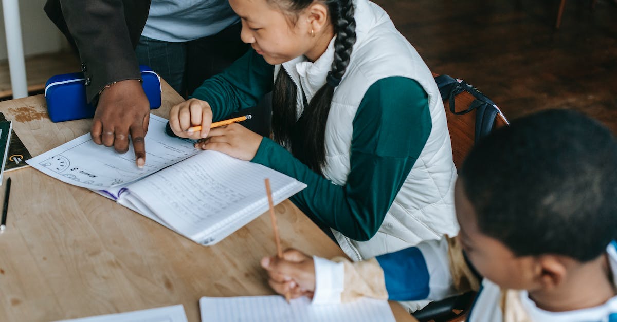 What's the point of Assignments? - Crop African American teacher standing near desk with diverse classmates and pointing at schoolgirls copybook