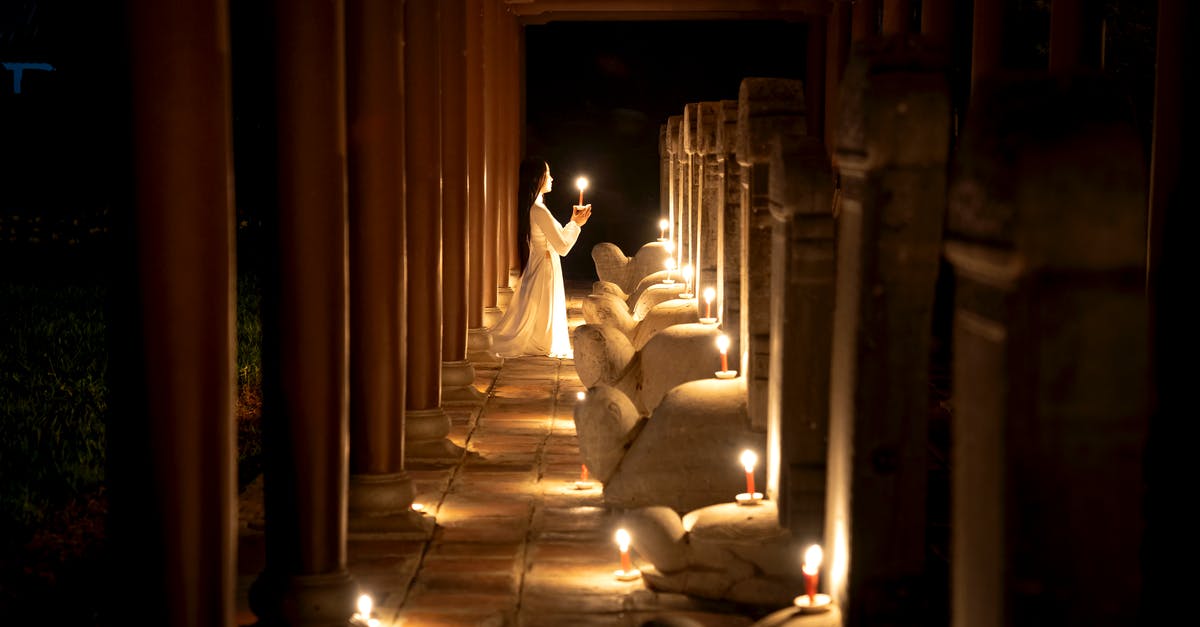 What's with the peaceful demonic statues in Dark Souls? - Side view of unrecognizable female with long dark hair in white dress standing on knees with burning candle near statue in temple in darkness