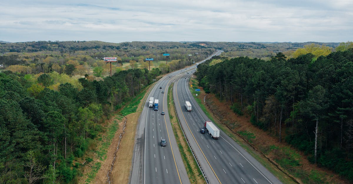 What affects the driving of the truck directly? - Aerial view of wavy asphalt roads with driving cars and trucks between bright trees under endless cloudy sky in rural zone