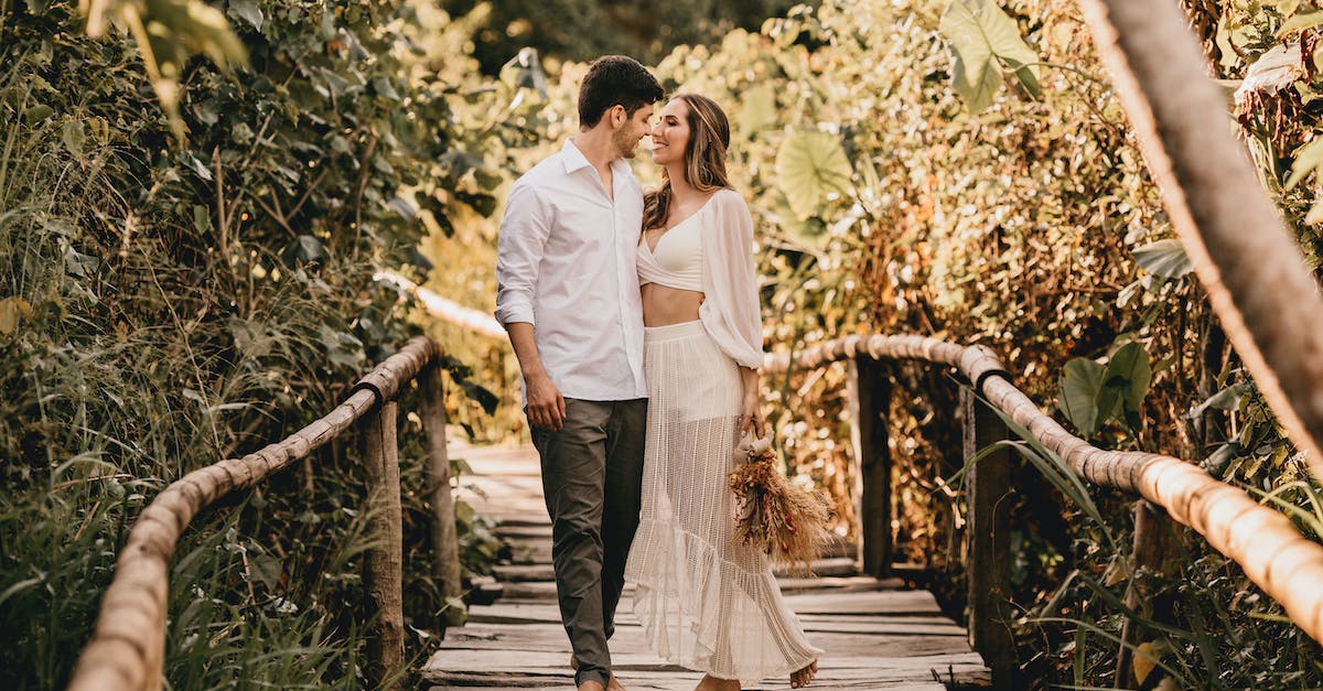 What affects the path of the ball after impact? - Full body of young couple in stylish clothes walking on wooden footbridge and looking at each other while spending time together on summer day What affects the path of the ball after impact? - Full body of young couple in stylish clothes walking on wooden footbridge and looking at each other while spending time together on summer day