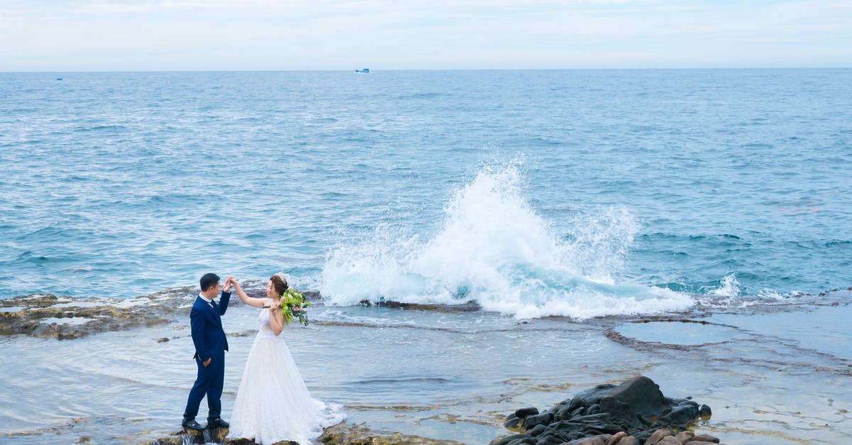 What affects your credit score in Endless Sky? - From above side view of anonymous bride in wedding dress with flower bouquet holding hand of groom while standing near sea with splattering water and looking at each other