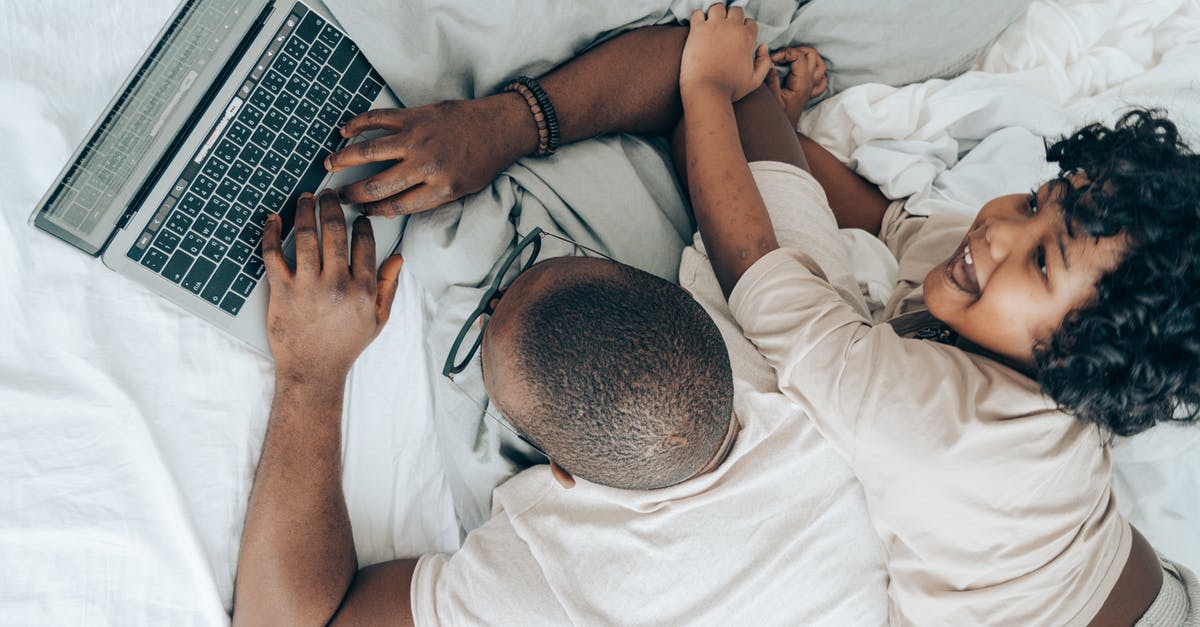 What are black belt and black glasses used for? - Top view of cheerful African American kid lying near father while man typing on keyboard of laptop during remote work in cozy bedroom