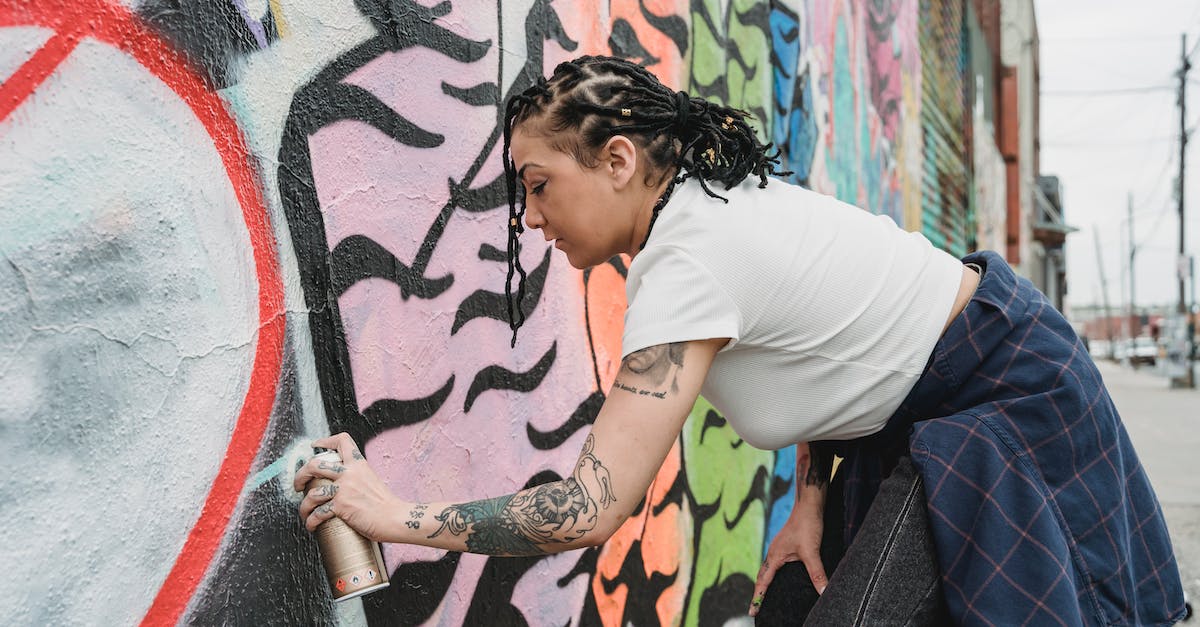 What are some skills that can hit targets outside their range? - Side view of focused ethnic female with tattoos spraying white paint on graffiti wall while standing on street of city