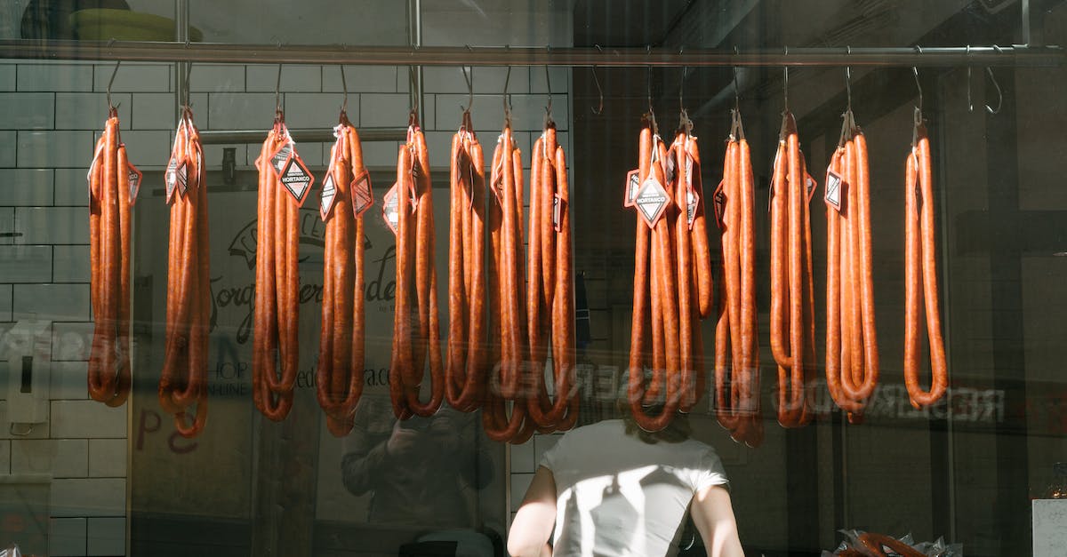 What are the benefits of fresh produce, and how long does it last? - Through glass back view of unrecognizable worker in white T shirt at meat preserving factory with long sausages hanging from metal rail in tiled room