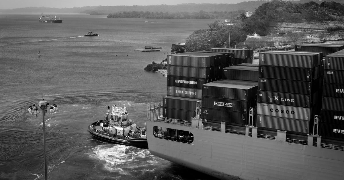 What are the benefits of having a cargo freight station? - Black and white contemporary cargo vessel with many containers floating on calm river near hilly grassy shore towards industrial port What are the benefits of having a cargo freight station? - Black and white contemporary cargo vessel with many containers floating on calm river near hilly grassy shore towards industrial port
