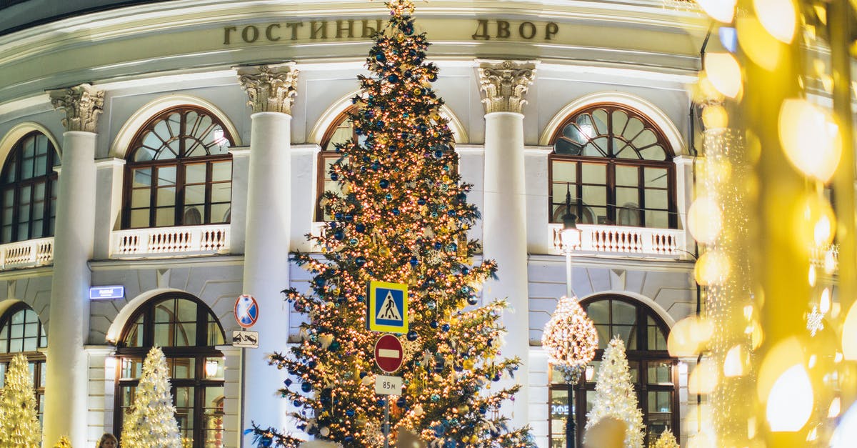 What are the big stars after leaving a station? - Low angle of decorated Christmas tree with blue and golden toys and glowing lamps on street against exterior of old building in evening city