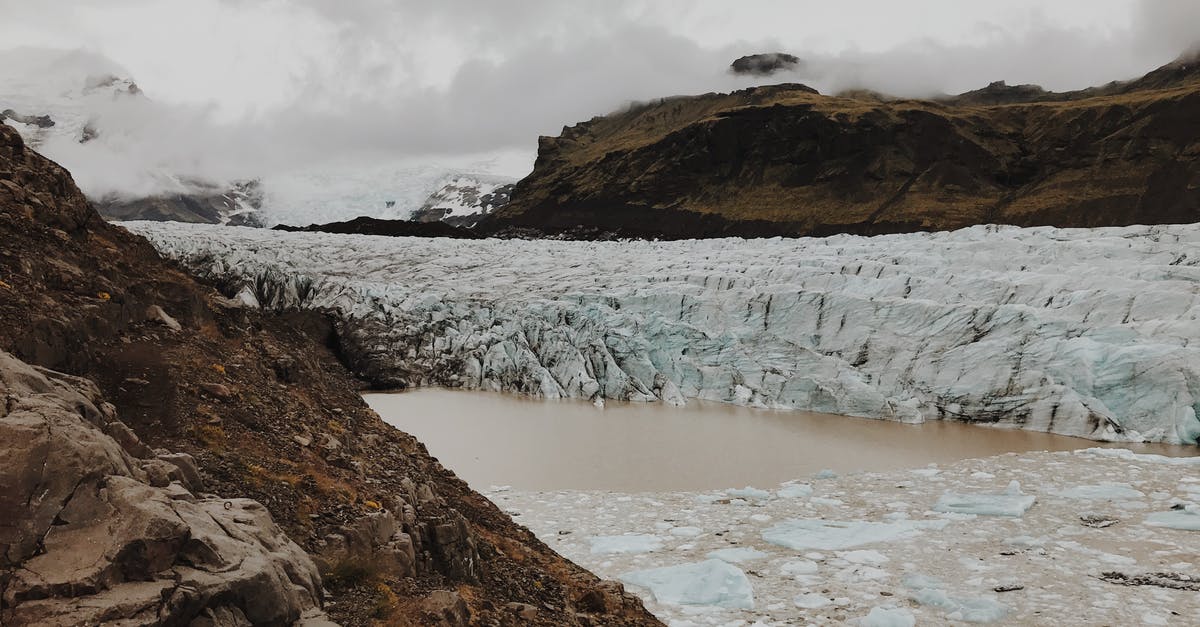 What are the Clouds floating in the foreground? - Brown Rock Formation Near Hill