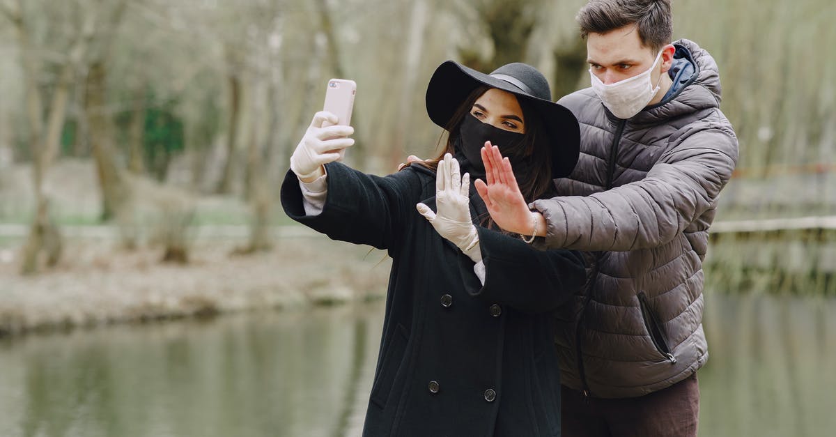 What are the consequences of using nuclear weapons against pirates or barbarians? - Serious couple in outwear wearing surgical gloves and masks taking selfie on smartphone and showing stop gesture while standing near lake in spring park during coronavirus pandemic
