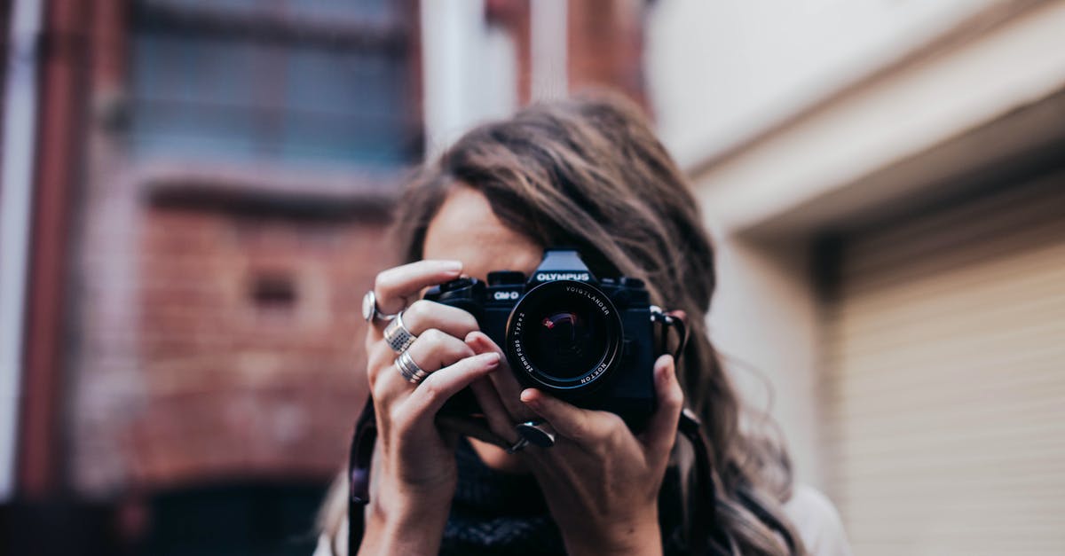 What attributes should a samurai build focus on in Elden Ring? - Unrecognizable female photographer taking photo and covering face with camera while standing on street against brick building on blurred background