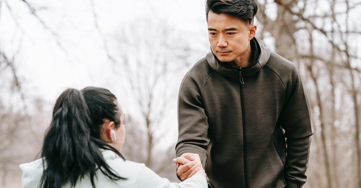 What could help give the 'wobbly' status in Pokemon Rumble world? - Calm Asian man in sportswear giving hand to unrecognizable female with dark hair in earphones in autumn park in daytime
