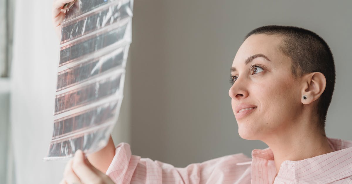 What decreases the negative exp effect on jobs - Side view of positive young female photographer watching filmstrip and smiling standing near window in light studio