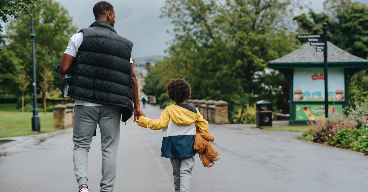 What direction to walk in to capture a targeted Pokemon? - Back view of anonymous African American man holding child by hand while walking on urban roadway in daylight