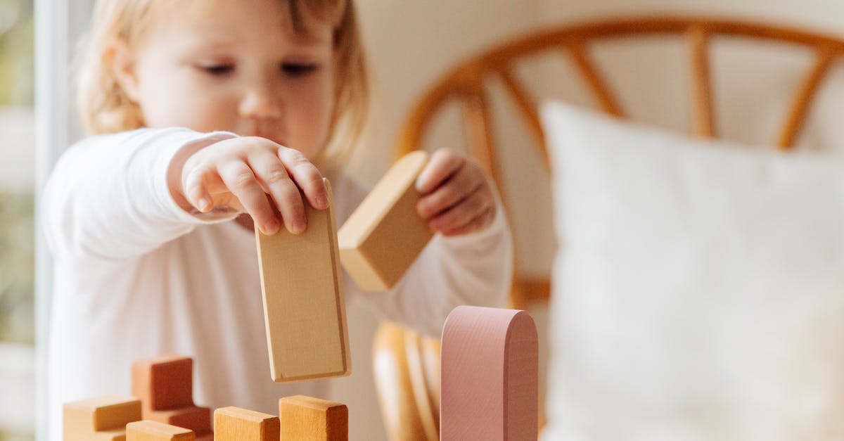 What does BM stand for in Gaming? - Cute little girl in white casual clothes standing near table and playing with wooden blocks while spending time at home