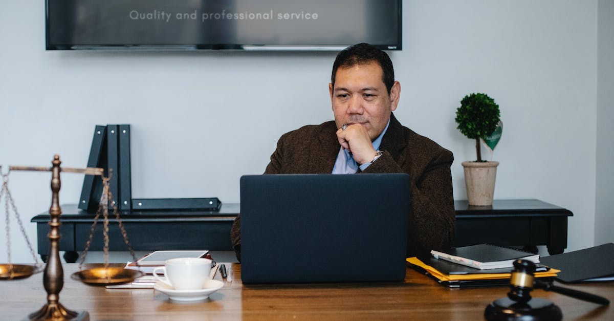 What does intelligence do in middle manager of justice? - Serious ethnic mature man in formal outfit working with netbook at table with gavel