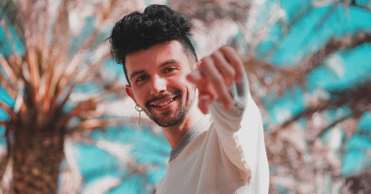 What does the arrow mean when you pick up a weapon? - Low angle of modern trendy man with earring pointing with finger at camera standing under palm trees in sunshine