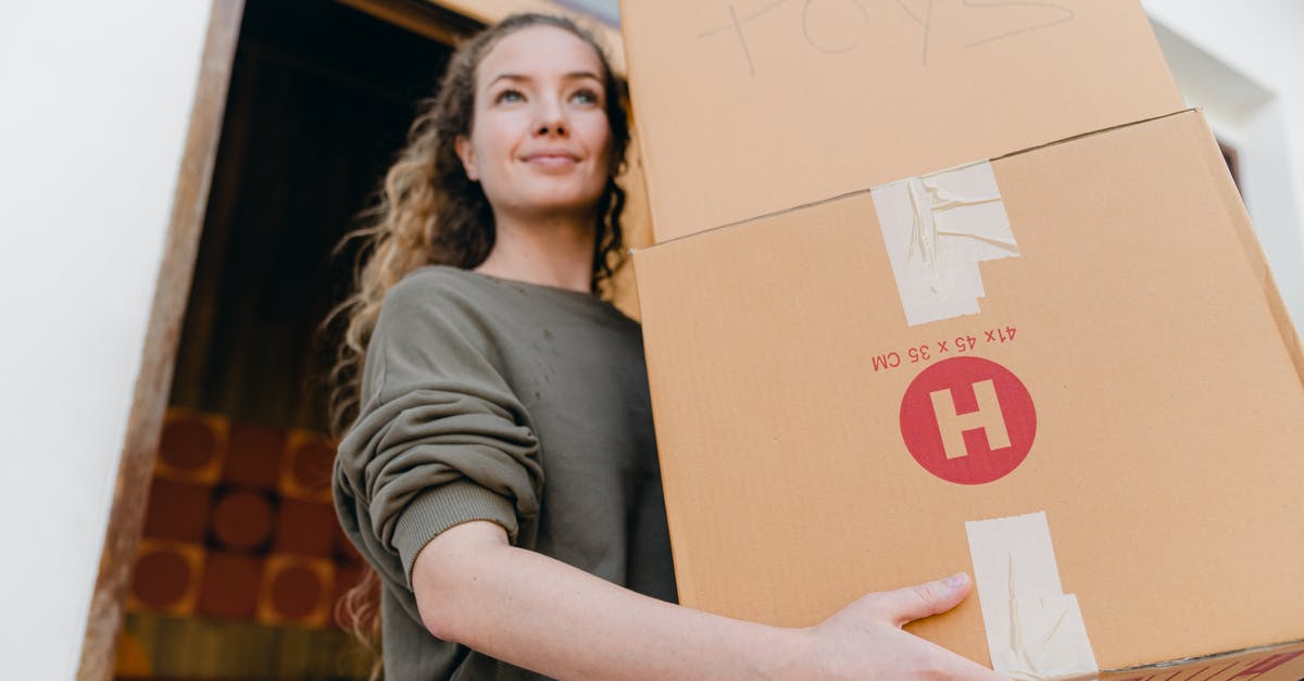 What does the door want from me? - Confident young lady in casual wear carrying heavy carton boxes with toys and looking away while leaving old house