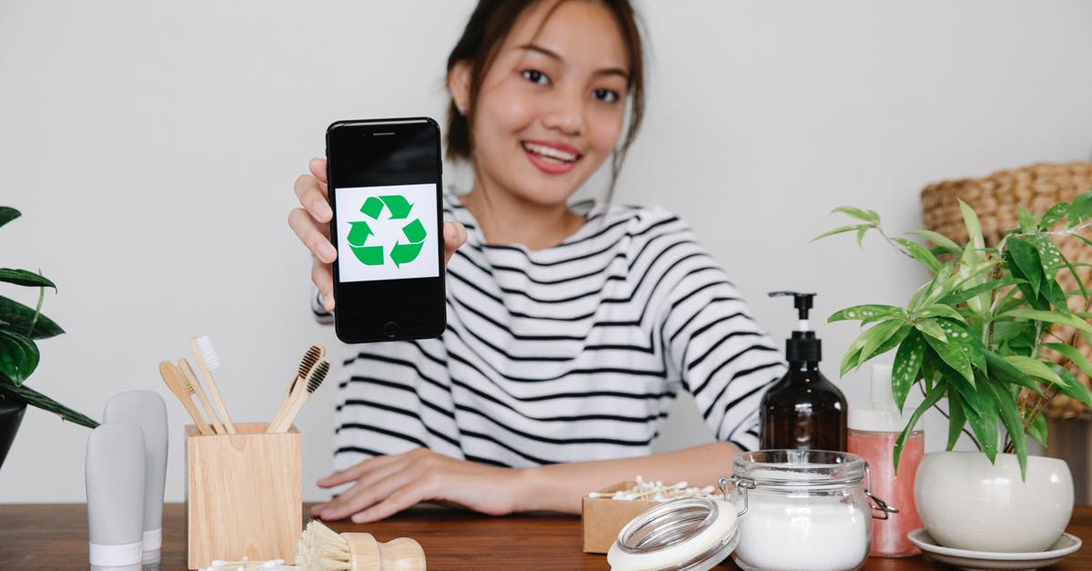 What does the Recycling Box do? - Smiling Asian woman demonstrating recycling symbol on smartphone while sitting at table with eco friendly cosmetic products and looking at camera What does the Recycling Box do? - Smiling Asian woman demonstrating recycling symbol on smartphone while sitting at table with eco friendly cosmetic products and looking at camera