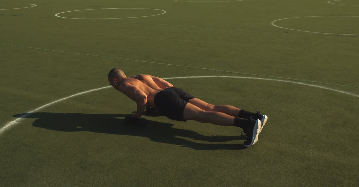 What does the shadow do? - Man in Black Shorts Doing Push Ups on Green Field