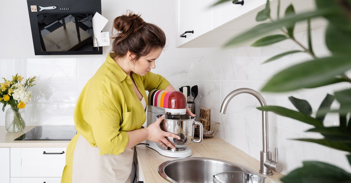 What does the T stand for in Tap Titans? - Side view of housewife in apron standing in kitchen and using food processor near sink