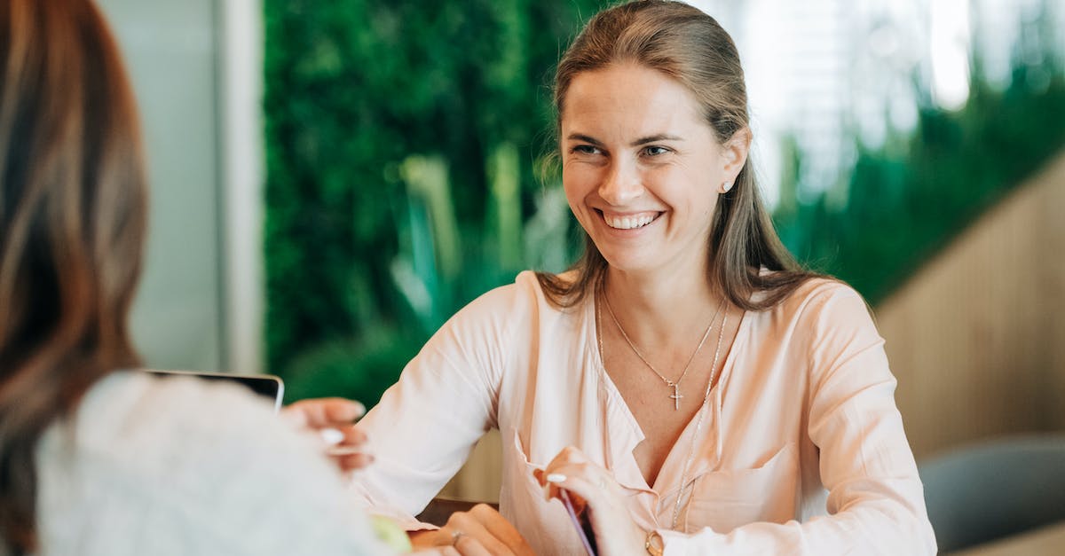 What does this green/white icon in clan chat mean? - Cheerful young female speaking with crop anonymous friend on blurred background of cafe with green plants
