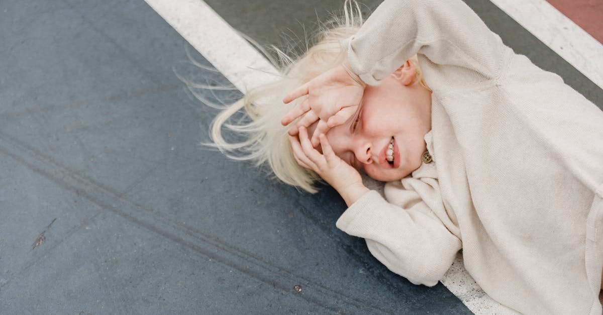 What effects does being on the high ground have? - From above of playful little blond kid in white shirt with closed eyes and hands on face lying on colorful sports ground What effects does being on the high ground have? - From above of playful little blond kid in white shirt with closed eyes and hands on face lying on colorful sports ground