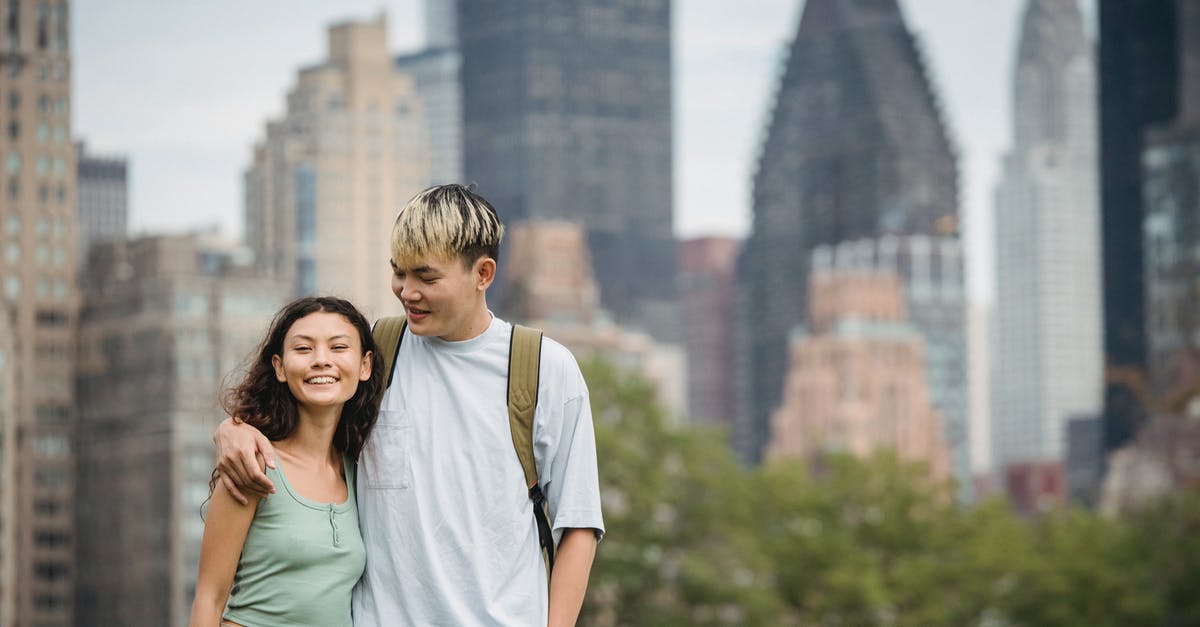 What factors affect a unit's contribution to city defense? - Cheerful young Asian couple in casual clothes hugging each other and standing against modern skyscrapers while spending holidays in New York