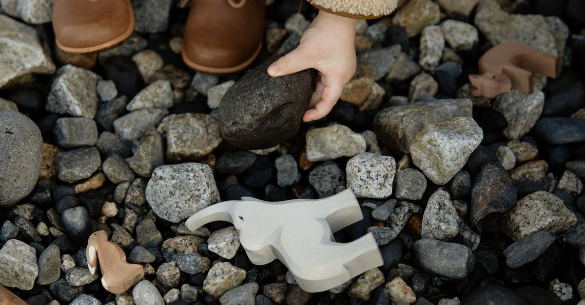 What game genre do these games fall into? - Unrecognizable crop kid playing with toys and stones on rocky ground