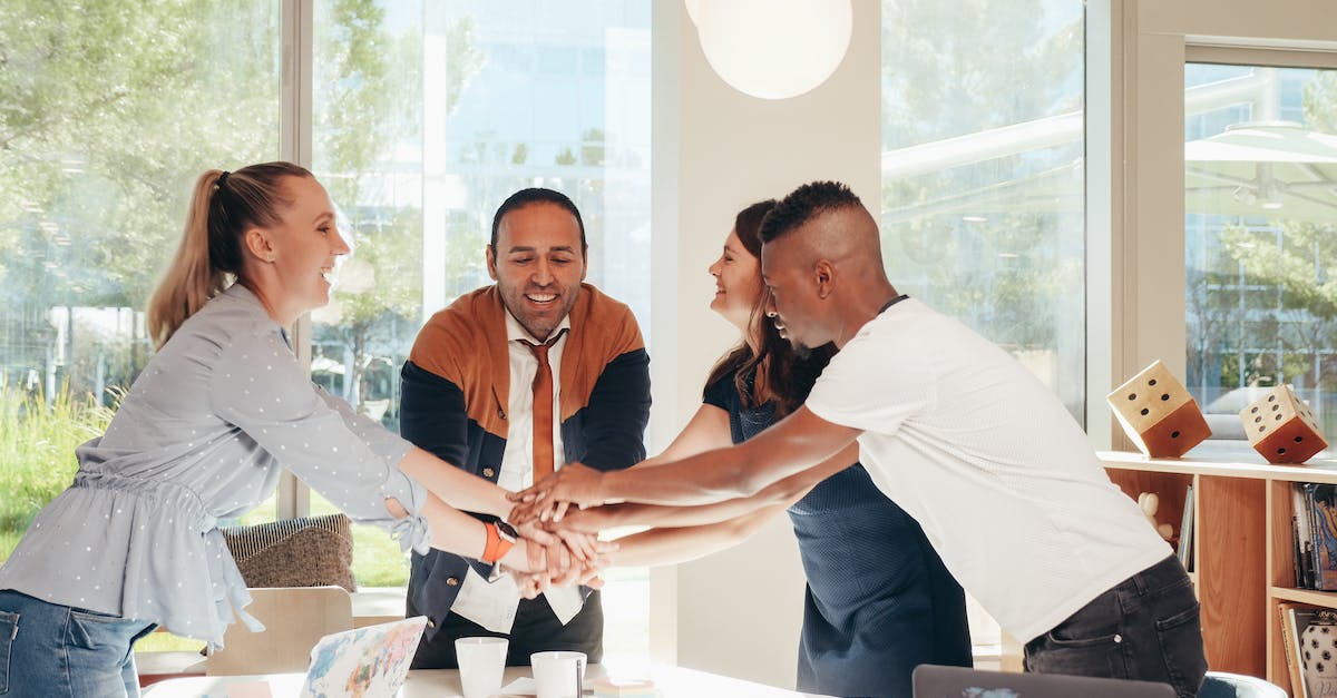 What happens to survivors resources when they join your group? - Content multiethnic colleagues joining hands above table with laptops in modern office on sunny day