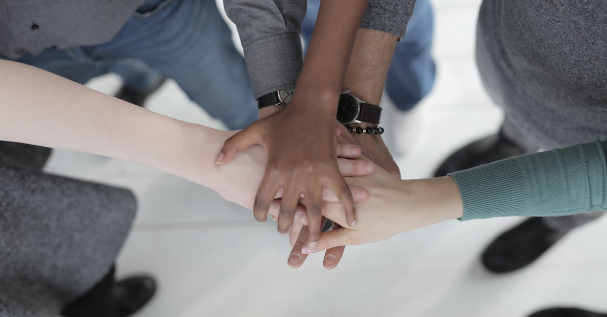 What happens to survivors resources when they join your group? - Crop from above of faceless multiracial friends in casual clothes uniting hands after coming to agreement while standing on light grey ceramic floor