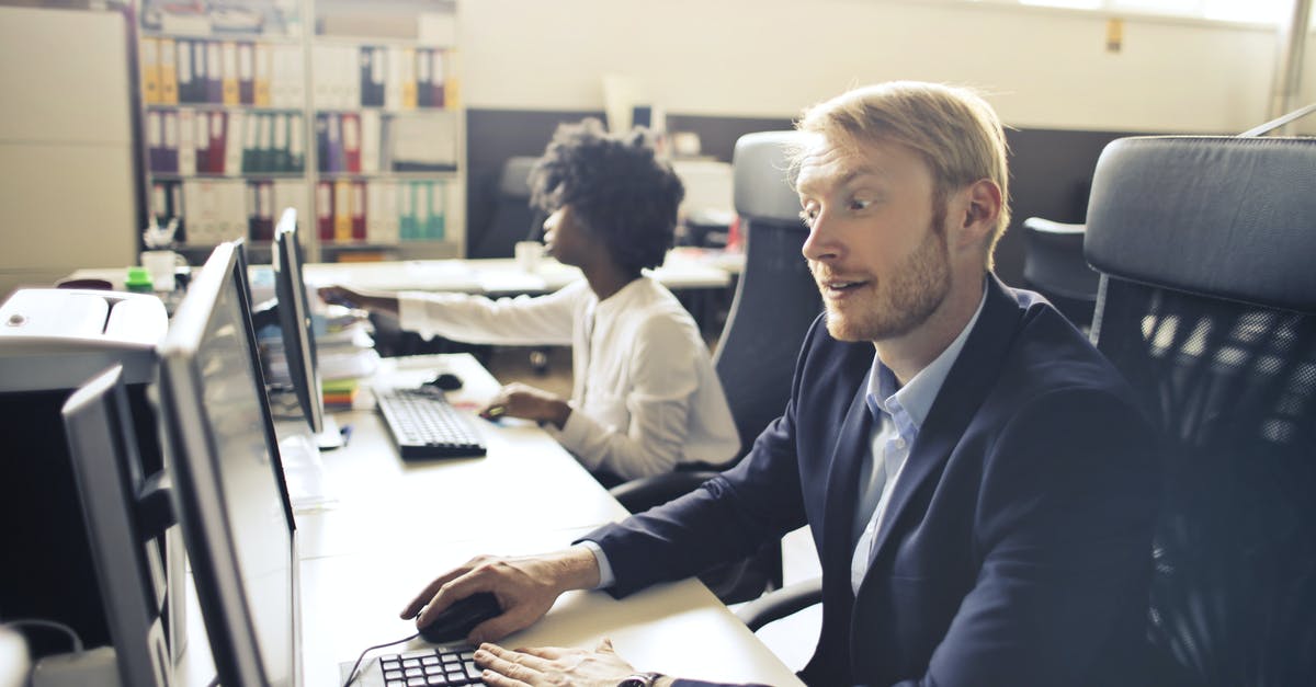 What happens when someone accessed you league account on another computer? - High angle of pensive shocked businessman in elegant clothes focusing on screen and interacting with computer while sitting at table near African American female coworker in light spacious office