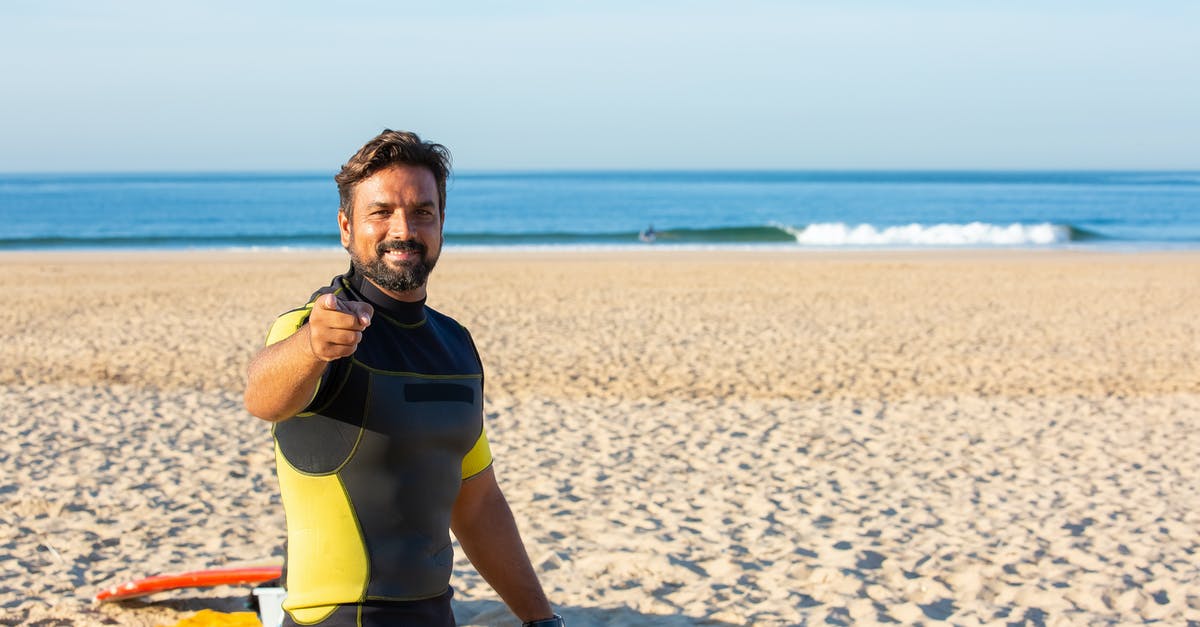 What happens when you pick up rune, when you already have one bottled - Happy male in diving suit looking and pointing at camera while standing on beach in bright sunny day