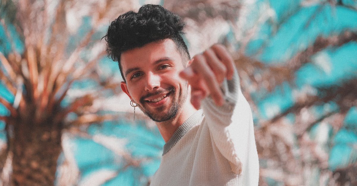What happens when you pick up rune, when you already have one bottled - Low angle of modern trendy man with earring pointing with finger at camera standing under palm trees in sunshine