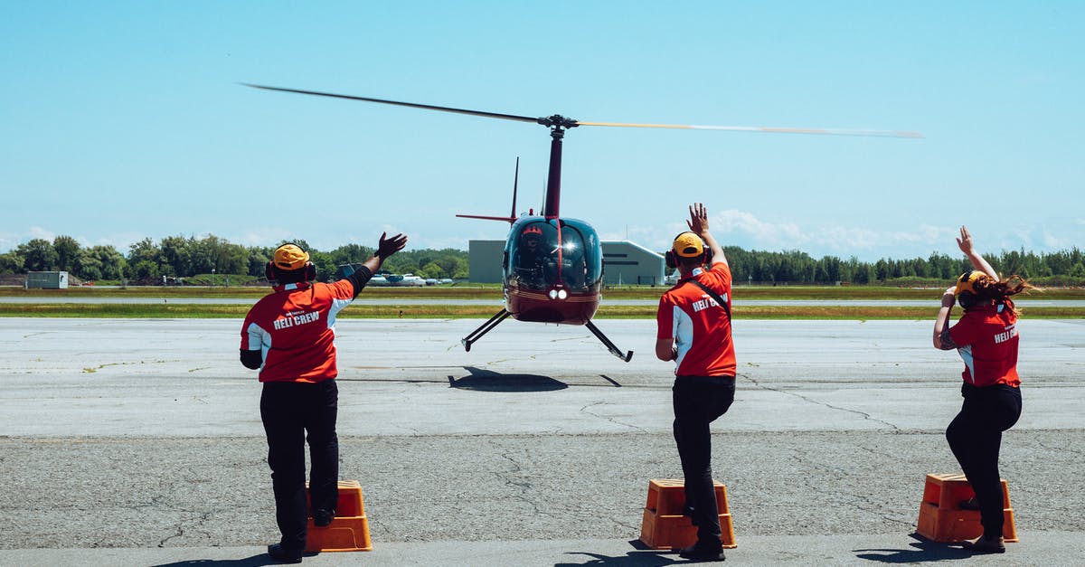 What happens when your crew is full and you're awarded a new crew member? - Back view of anonymous ground crews in uniforms and headsets meeting passenger helicopter on airfield after flight against cloudless blue sky